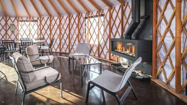A yurt interior with a central fire pit, seating arrangements, and a wooden lattice wall. - Hotel Rapids (Grand Rapids)