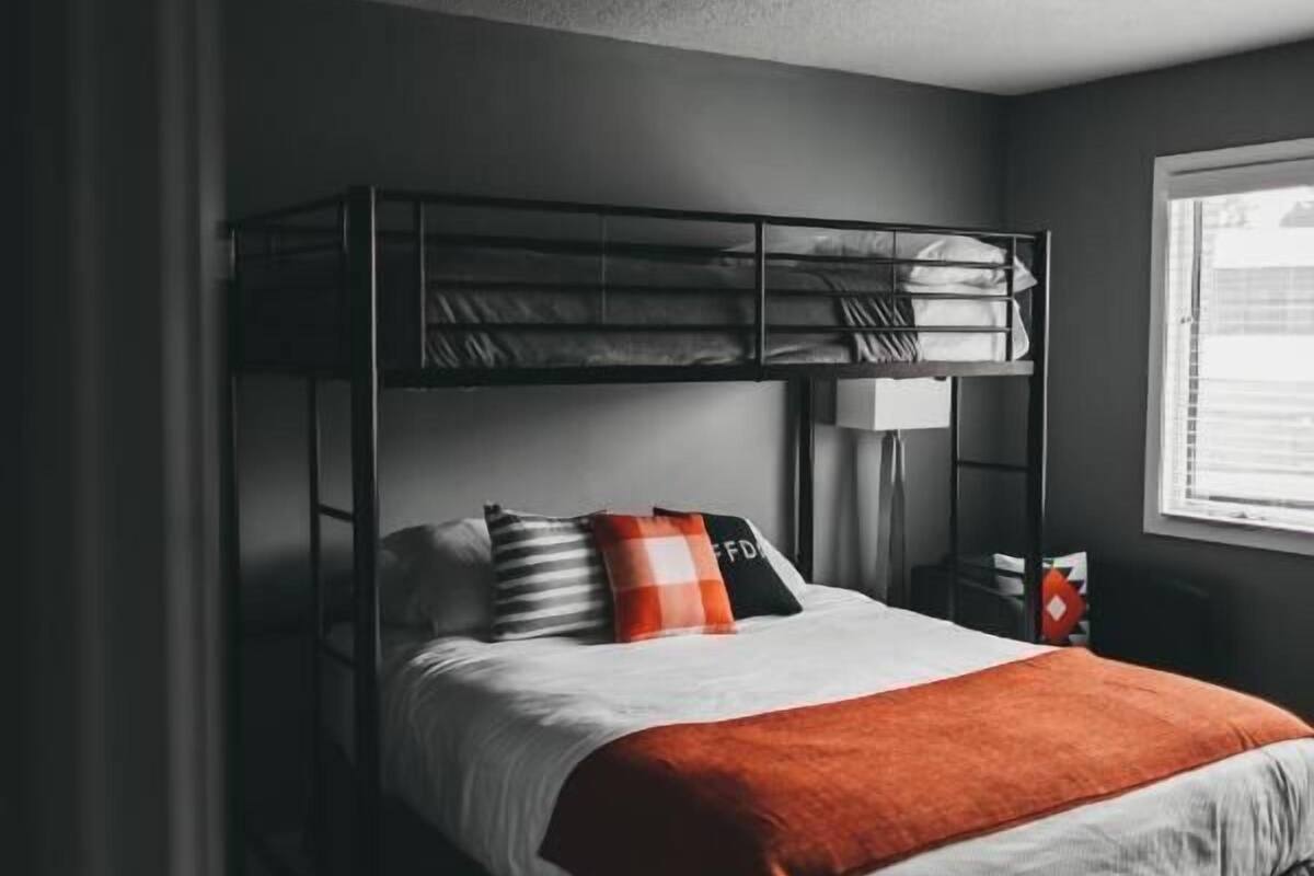 A bunk bed with a white mattress, orange blanket, and striped pillows.