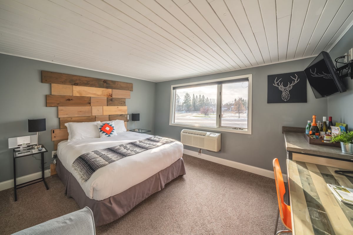 A bedroom with a bed, a desk, a chair, a TV, and a window with a view of trees.