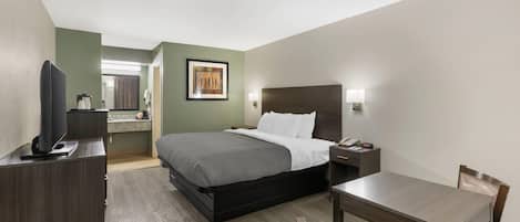 A hotel room with a bed, bedside table, chair, desk, television, and a painting on the wall.