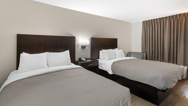 Habitación de hotel con dos camas individuales, una mesita de noche con teléfono y lámpara, y una ventana con cortinas.