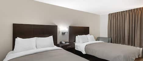 Habitación de hotel con dos camas individuales, una mesita de noche con teléfono y lámpara, y una ventana con cortinas.