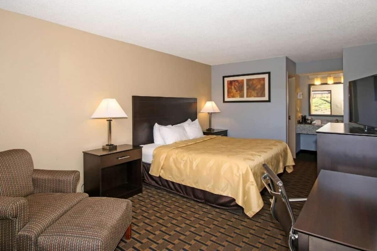 A hotel room with a bed, a chair, a desk, and a mirror.