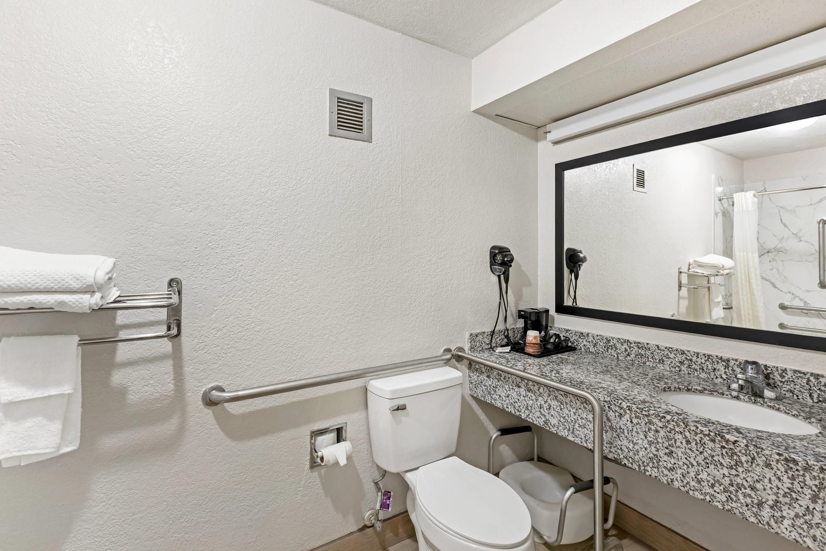 A bathroom with a white toilet, a sink with a granite countertop, a mirror, and a towel rack.
