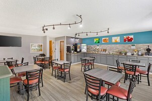 A restaurant with multiple tables and chairs, a kitchen area, and a wall with food images.