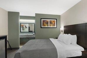 A hotel room with a bed, a nightstand, a mirror, a framed abstract painting, and a bathroom visible through an open door. - Quality Inn Clinton - Laurens I-26 (Clinton)