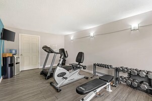 Un gimnasio en casa con cinta de correr, bicicleta estática, banco y mancuernas.