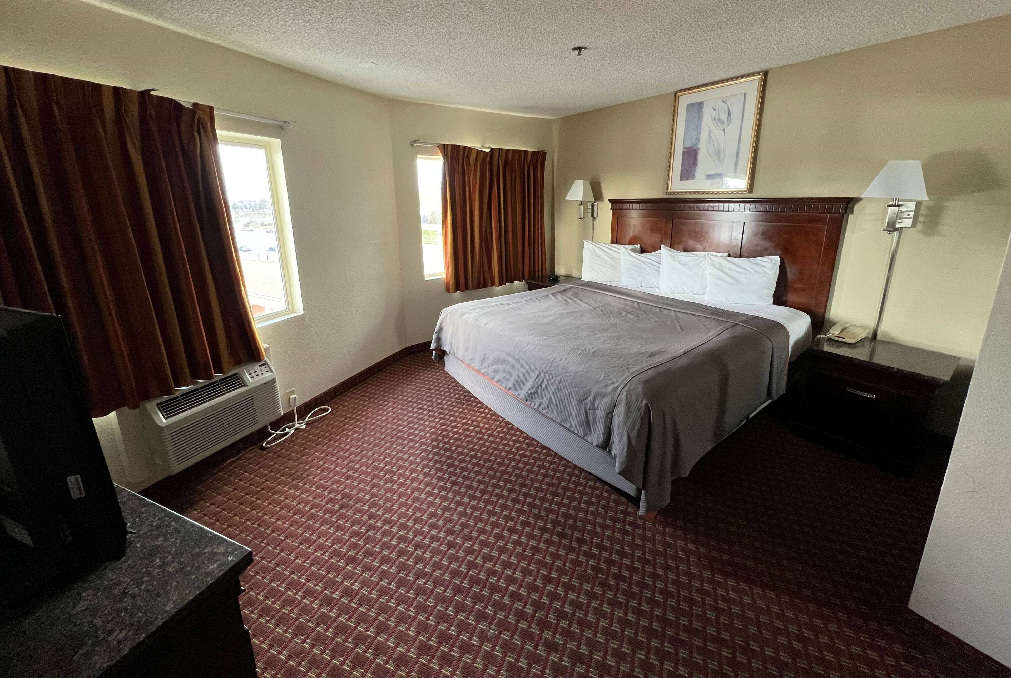Habitación de hotel con cama, escritorio, silla, lámpara y ventana con cortinas.
