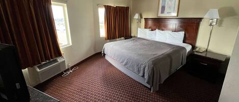 Habitación de hotel con cama, escritorio, silla, lámpara y ventana con cortinas.
