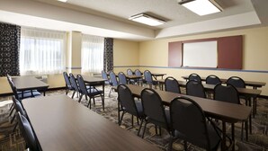 Ein Konferenzraum mit mehreren Tischen und Stühlen, einer Projektionsleinwand und einem Teppichboden.