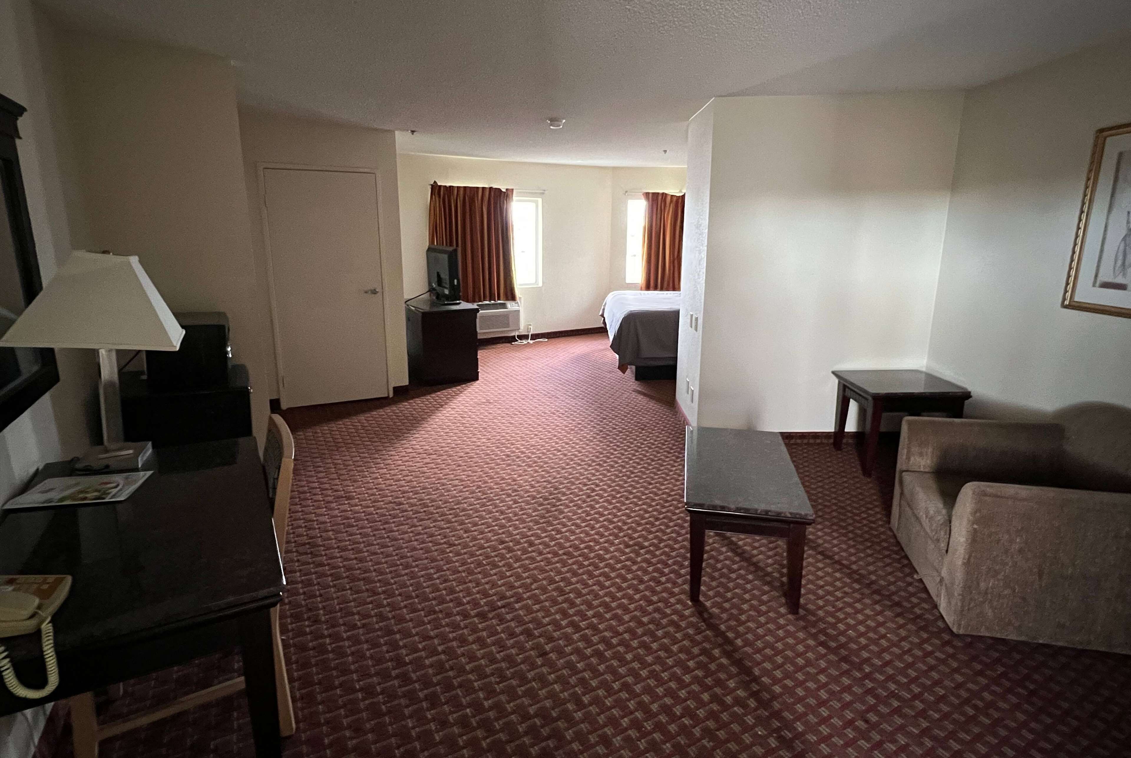 A hotel room with a bed, a desk with a lamp, a chair, a small table, and a sofa.