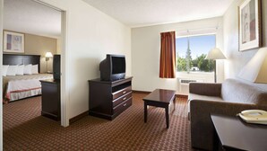 Ein Hotelzimmer mit Bett, Fernseher auf einem Schminktisch, Schreibtisch, einer Couch und einem Fenster mit Vorhängen.