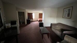 Ein Hotelzimmer mit Wohnbereich, einem Bett, einem Fernseher und einem Schreibtisch.