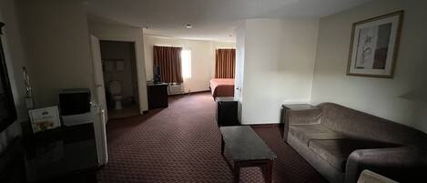 A hotel room with a living area, a bed, a television, and a desk.