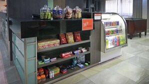 A snack vending machine with a 24/7 sign, various snack items, and a refrigerator with beverages. - Hampton Inn by Hilton Monterrey-Airport (Apodaca)