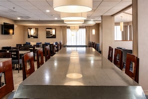 A long conference table with chairs, overhead lighting, and a television on the wall.