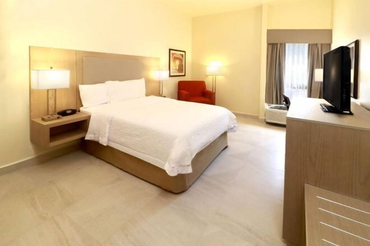 A hotel room with a bed, bedside lamps, a desk with a television, and a chair.