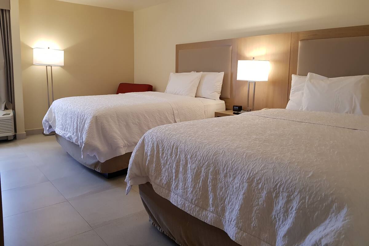 A hotel room with two beds, each with a headboard and bedside lamps.