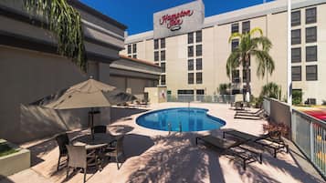 Zona de piscina con sillones de descanso y sombrillas en Hampton Inn.