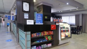 A hotel reception area with a self-service beverage machine, a refrigerated display case, and a seating area with a view of the windows. - Hampton Inn by Hilton Monterrey-Airport (Apodaca)