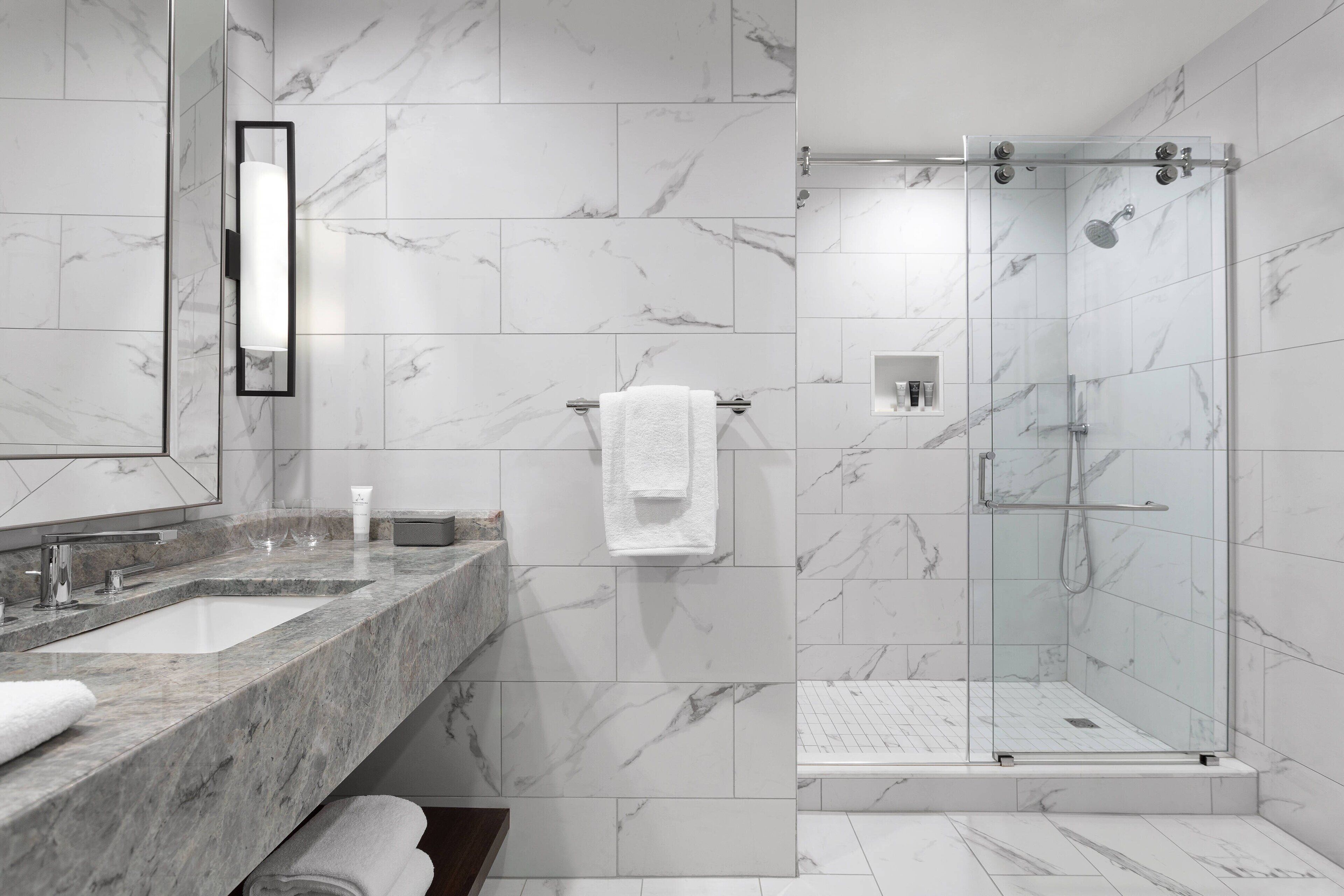 Une salle de bain moderne avec des carreaux de marbre, une douche à parois de verre et un grand miroir.