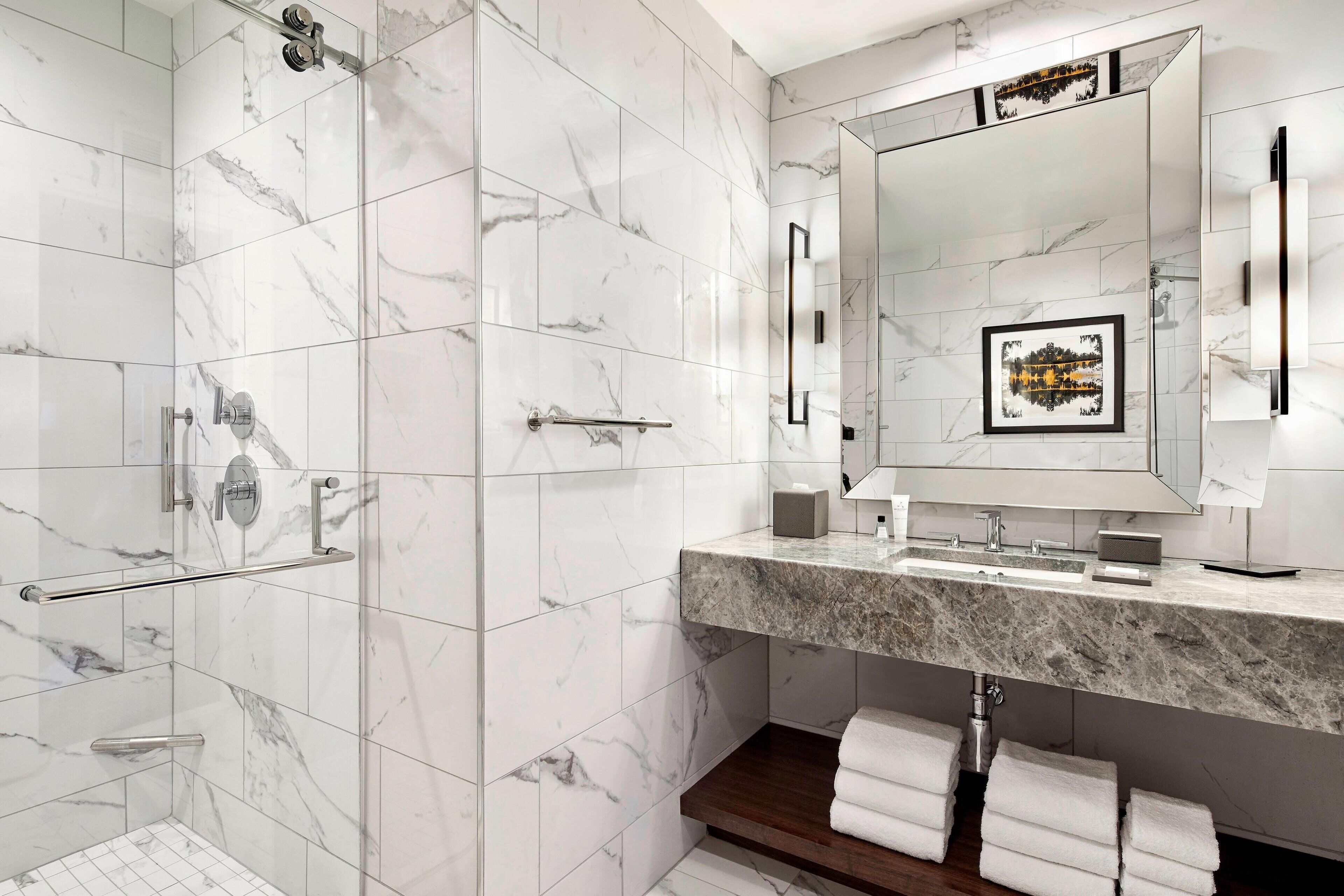 Un baño moderno con azulejos de mármol, un espejo grande, ducha y tocador con encimera de mármol.