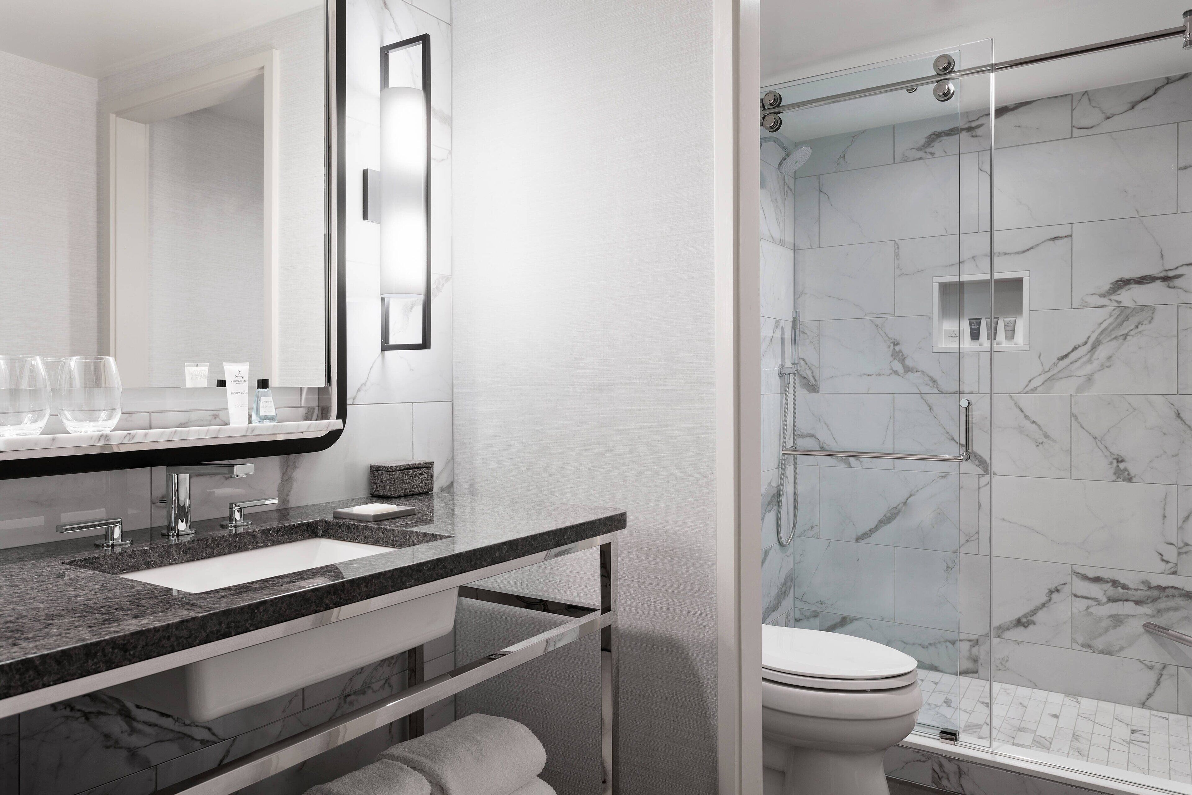 Une salle de bain moderne avec un lavabo en marbre, un grand miroir et une douche à parois de verre.