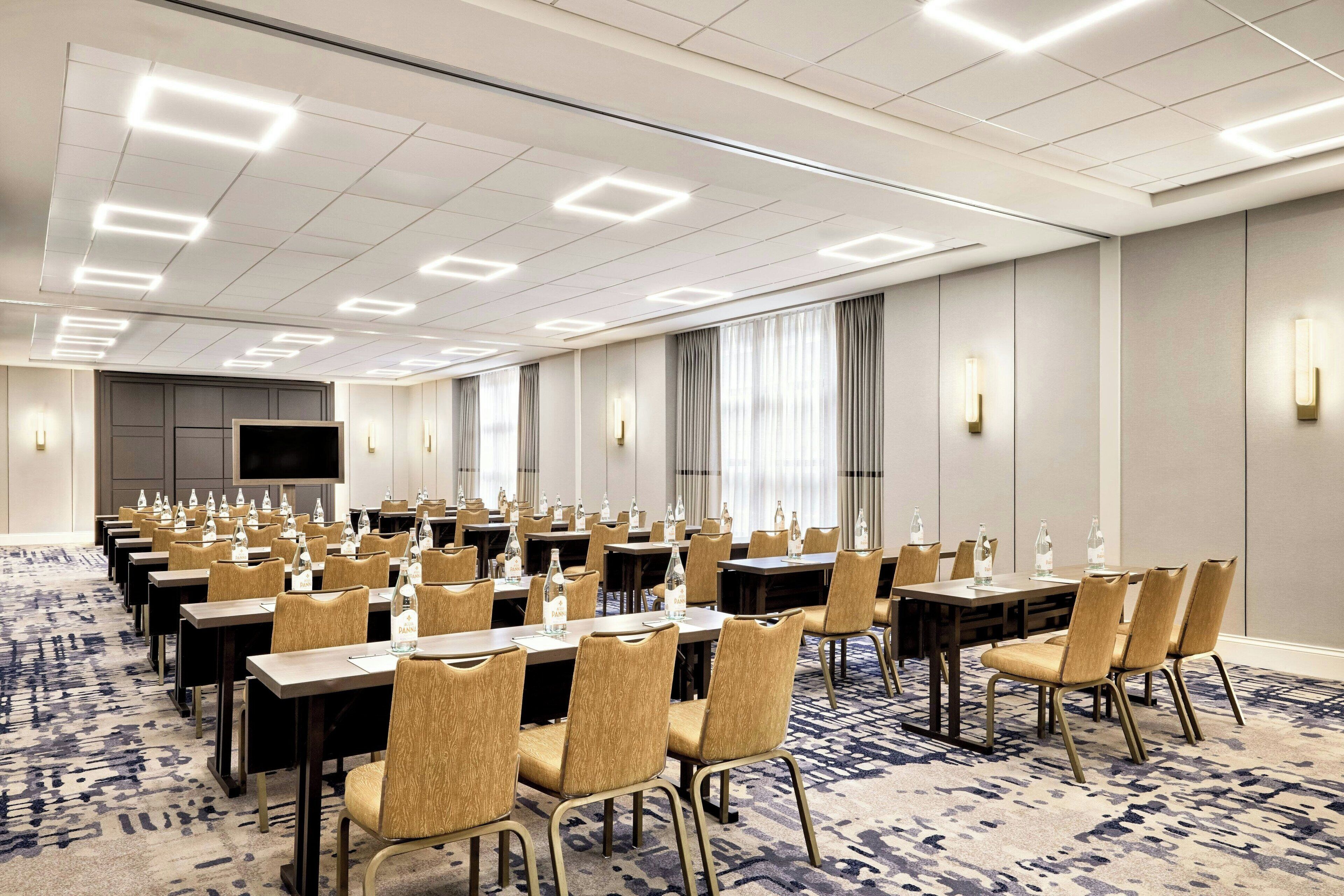 A conference room with multiple tables and chairs, equipped with water bottles and a large screen.