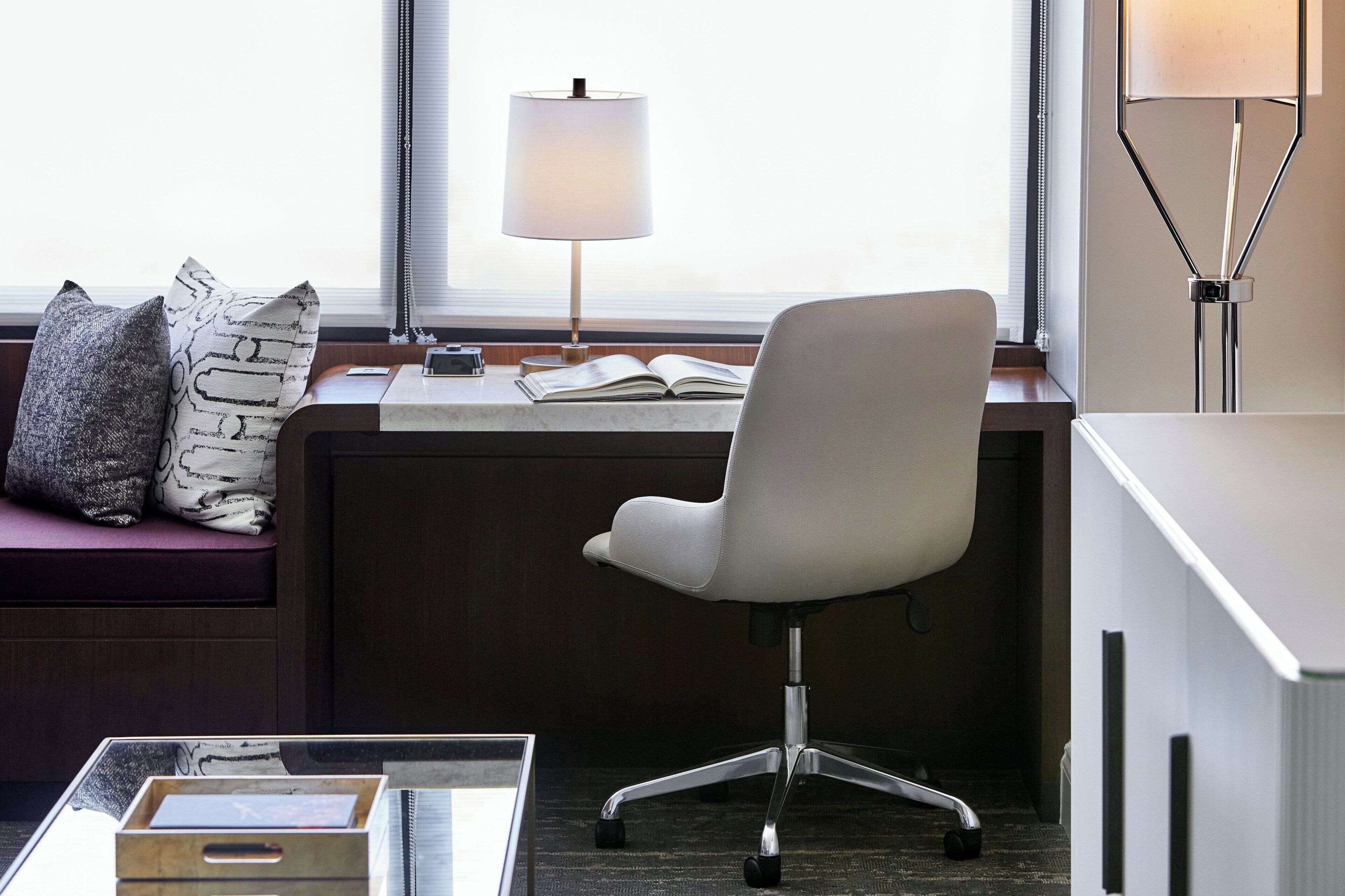 A modern office space with a white office chair, a desk with a lamp, and a window with blinds.