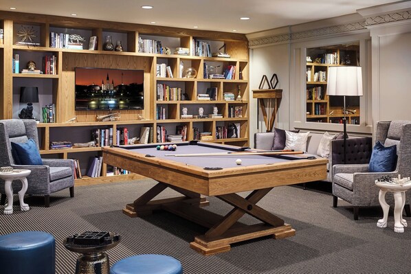 A cozy living room with a pool table, comfortable seating, and a large bookshelf filled with books and decorative items.
