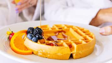 A breakfast plate with waffles, blueberries, orange slices, and a strawberry, with syrup being poured over it.