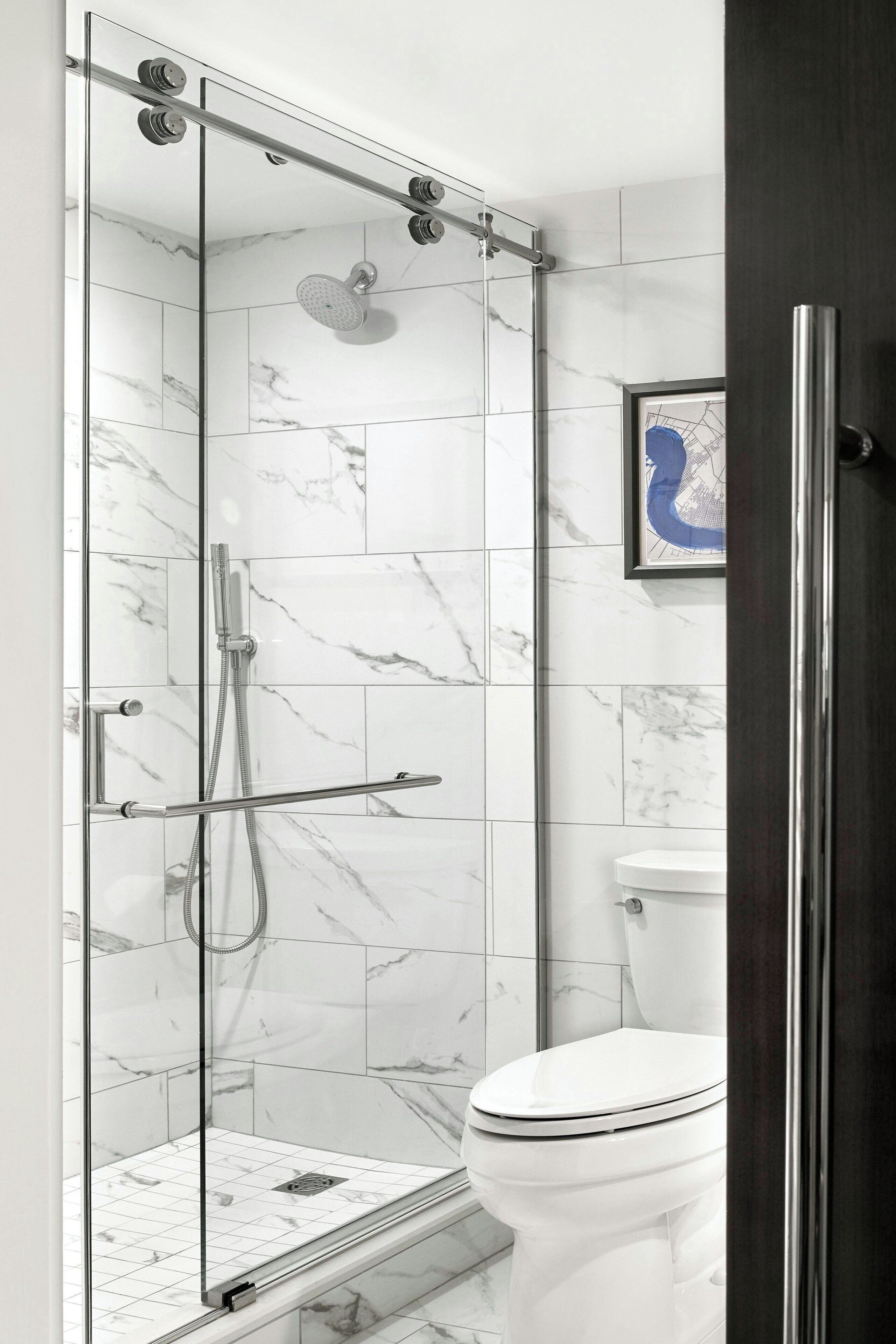 A modern bathroom with a glass-enclosed shower, white marble tiles, and a white toilet.