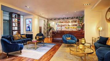 A modern living room with dark blue sofas, a glass coffee table, and a bar area with shelves of bottles and decorative items.