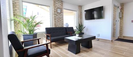 A modern lounge area with a sofa, chairs, a coffee table, and a TV mounted on the wall.