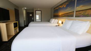 Quarto de hotel com duas camas, televisão, escrivaninha e uma pintura de pôr do sol.