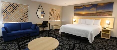 A hotel room with a bed, a blue sofa, a round table, and a desk with a chair.