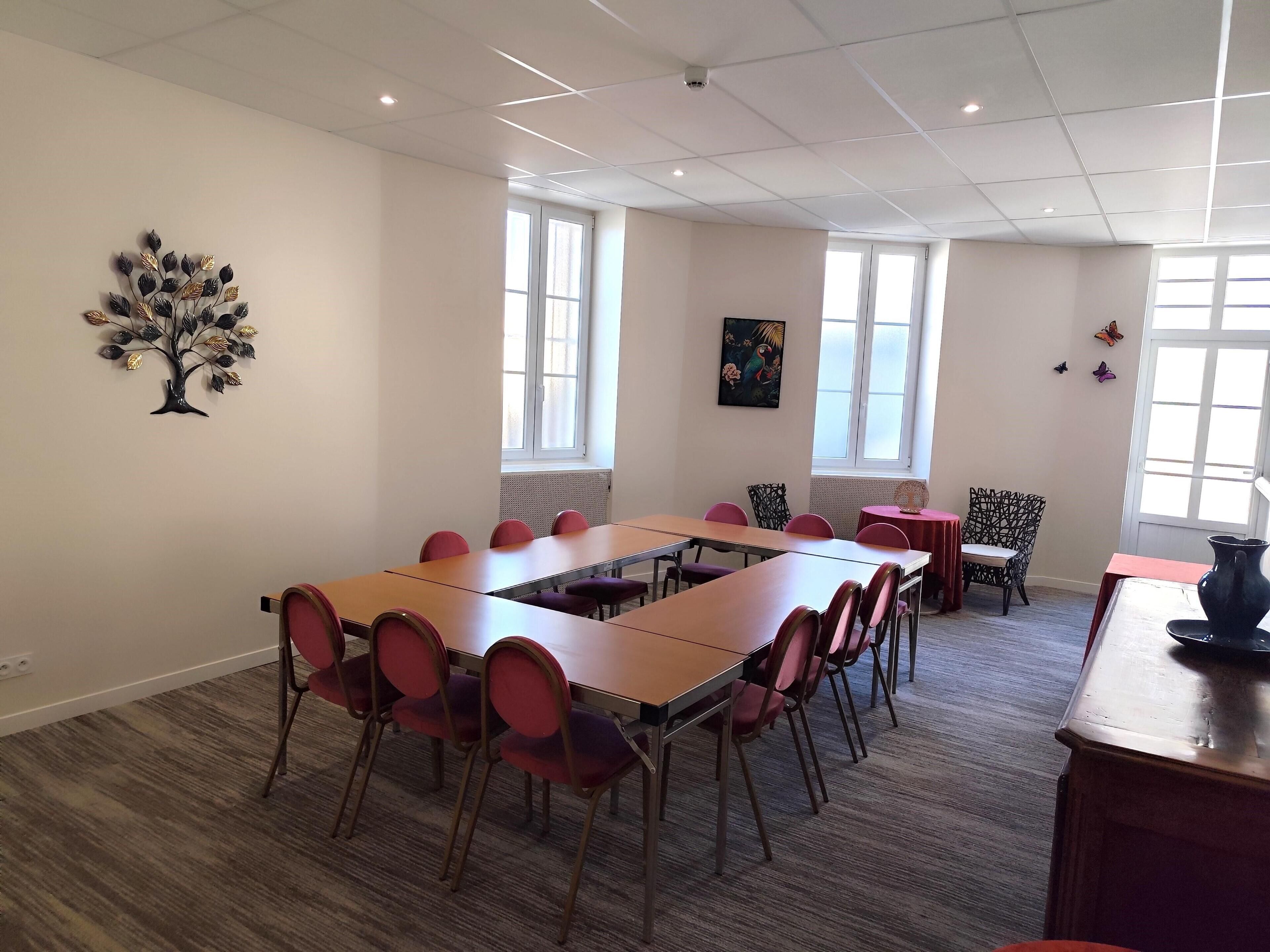 A conference room with a long table, red chairs, and a decorative tree on the wall.
