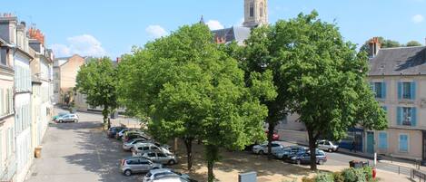 A street lined with parked cars and trees, with buildings on either side and a tower in the background.