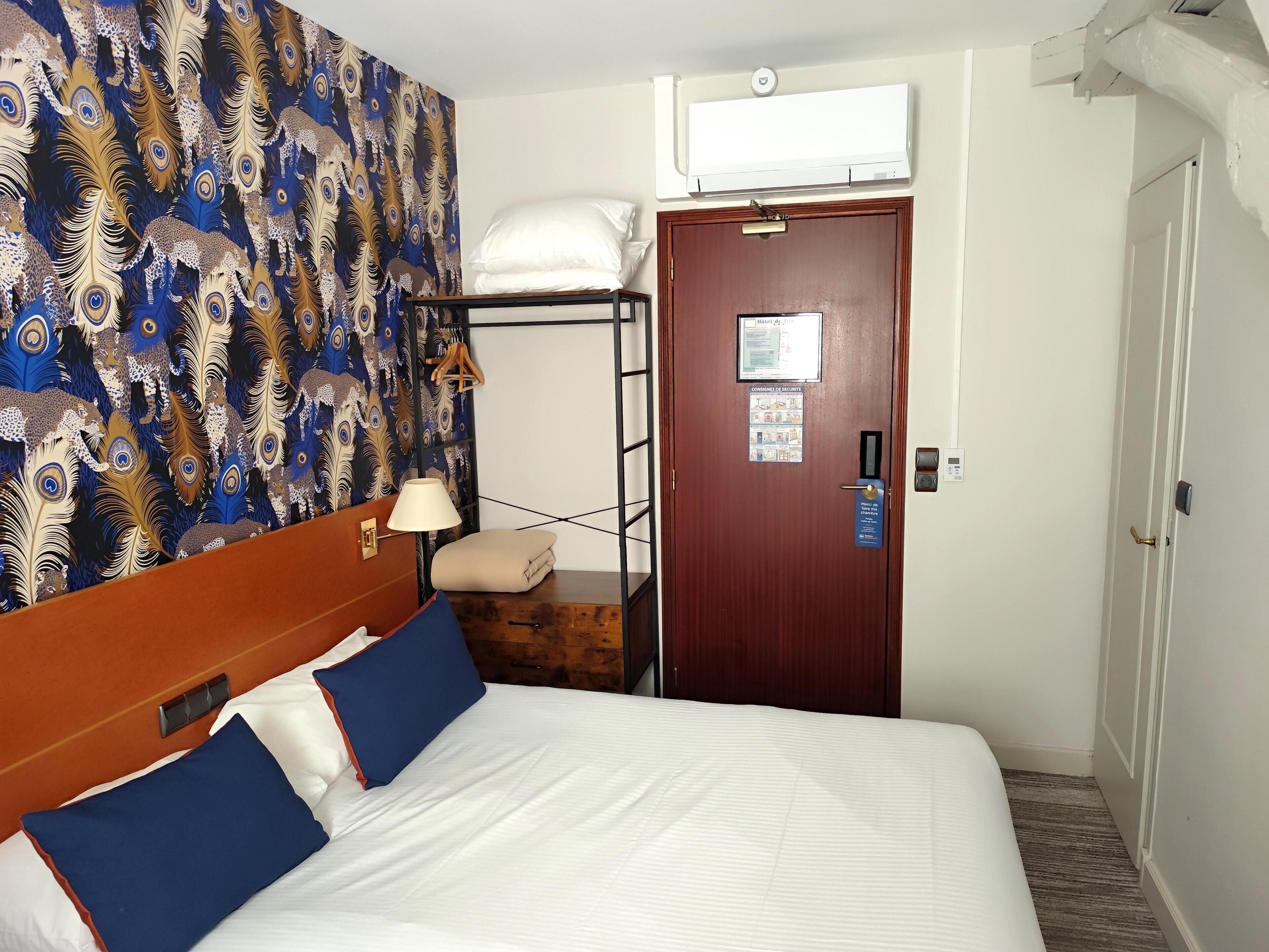 Ett hotellrum med en säng, en väggmonterad luftkonditioneringsanläggning, en dörr med en säkerhetsanvisning och en vägg med ett mönster.