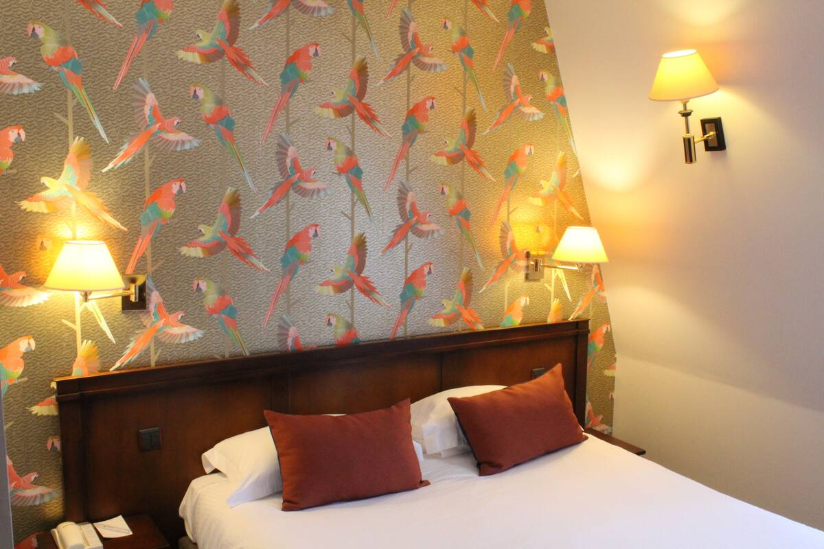 A hotel room with a bed, two pillows, a nightstand with a phone, and two wall-mounted lamps.