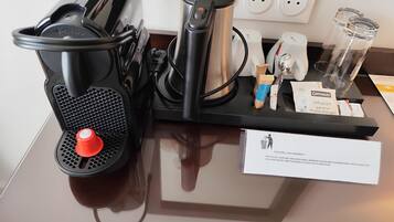 Une machine à café, une bouilloire et un distributeur d’eau sont posés sur un comptoir, à côté d’un panneau indiquant les consignes de tri.