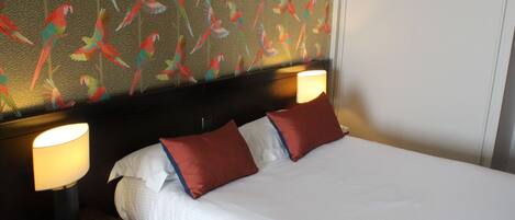 A hotel room with a large bed, two bedside lamps, and a wall with a parrot pattern.
