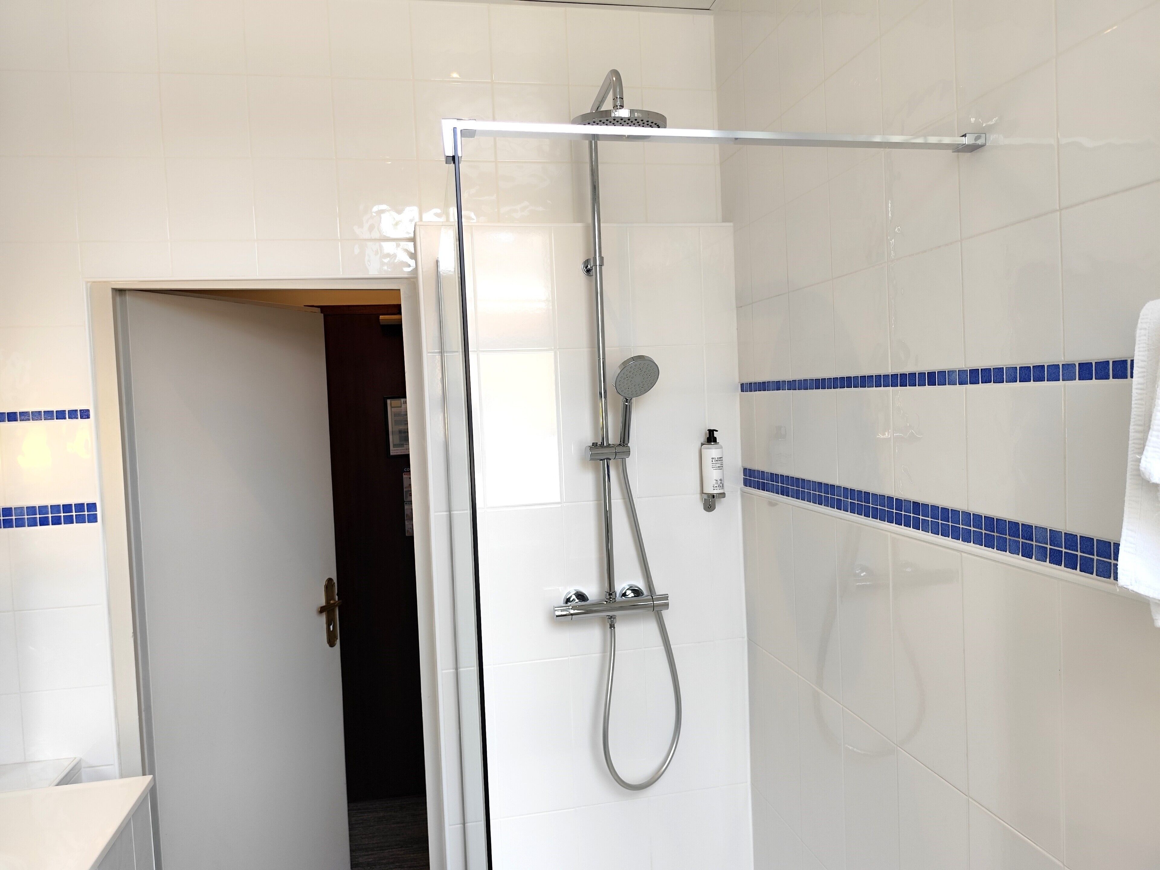 A bathroom with a shower, a towel rack, and a door leading to another room.