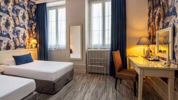 Quarto de hotel com duas camas, uma escrivaninha, uma cadeira, um espelho e um radiador.