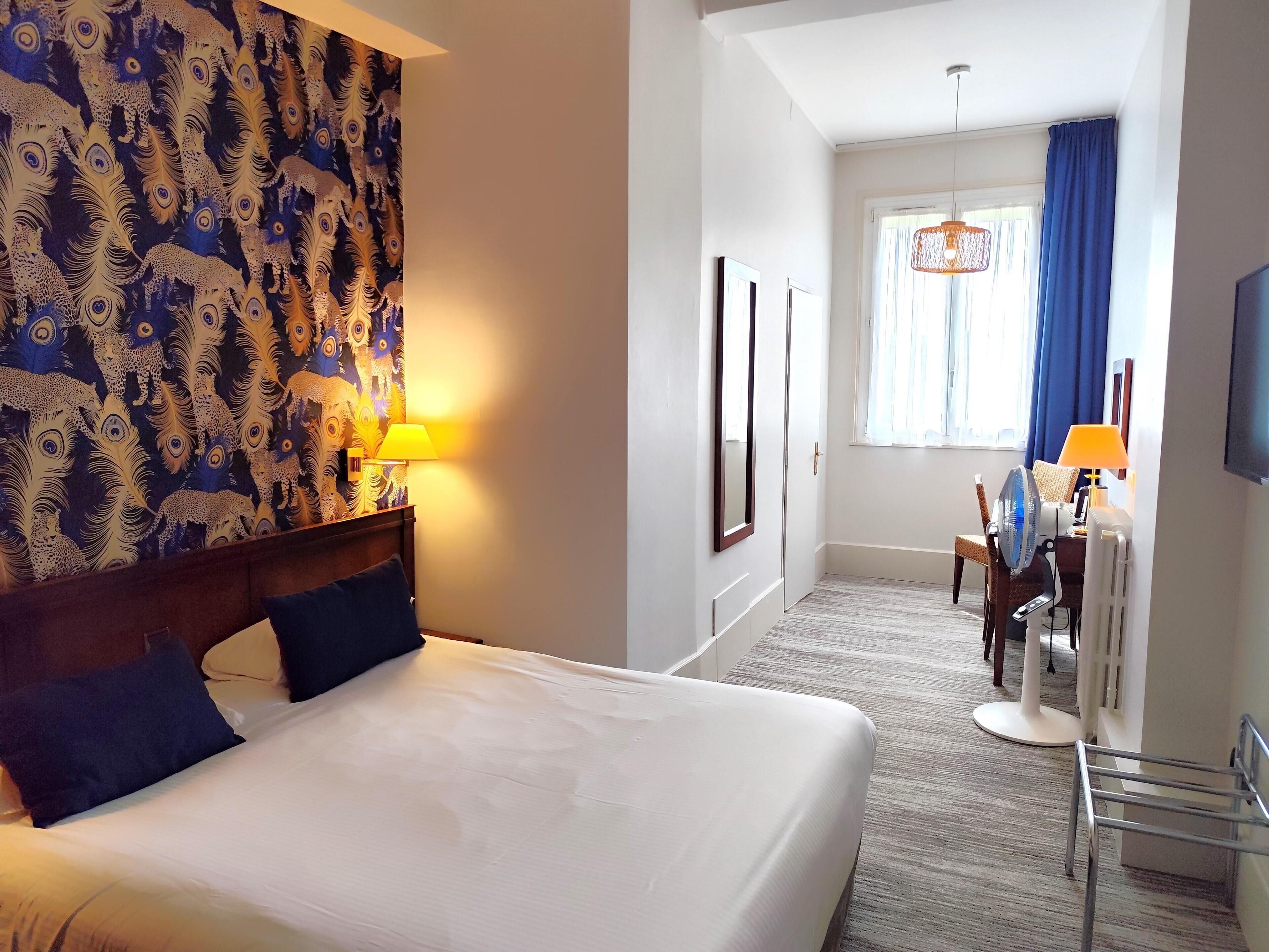 A hotel room with a large bed, a desk with a chair, a TV, and a window with curtains.