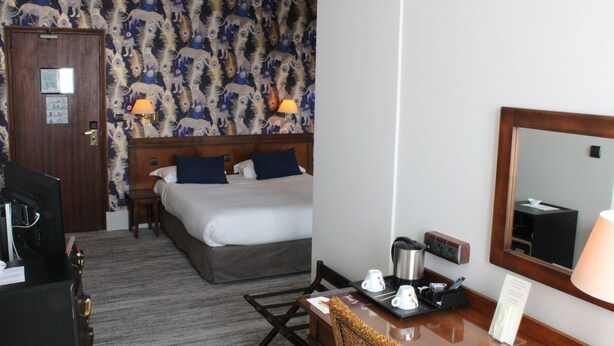 Habitación de hotel con cama, escritorio con lámpara, cafetera y espejo.