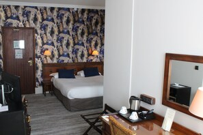Habitación de hotel con cama, escritorio con lámpara, cafetera y espejo.