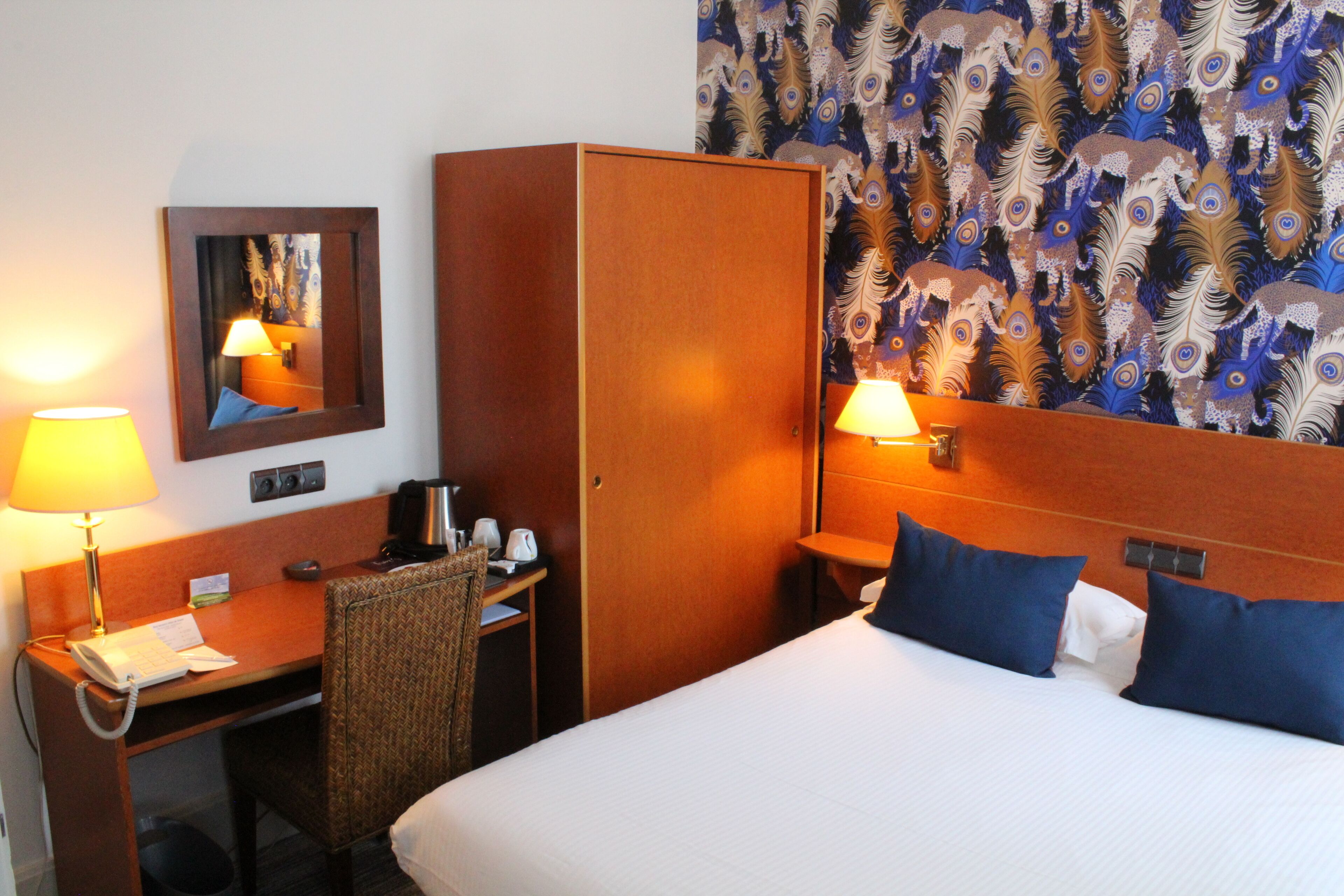 A hotel room with a bed, desk, chair, and a mirror.