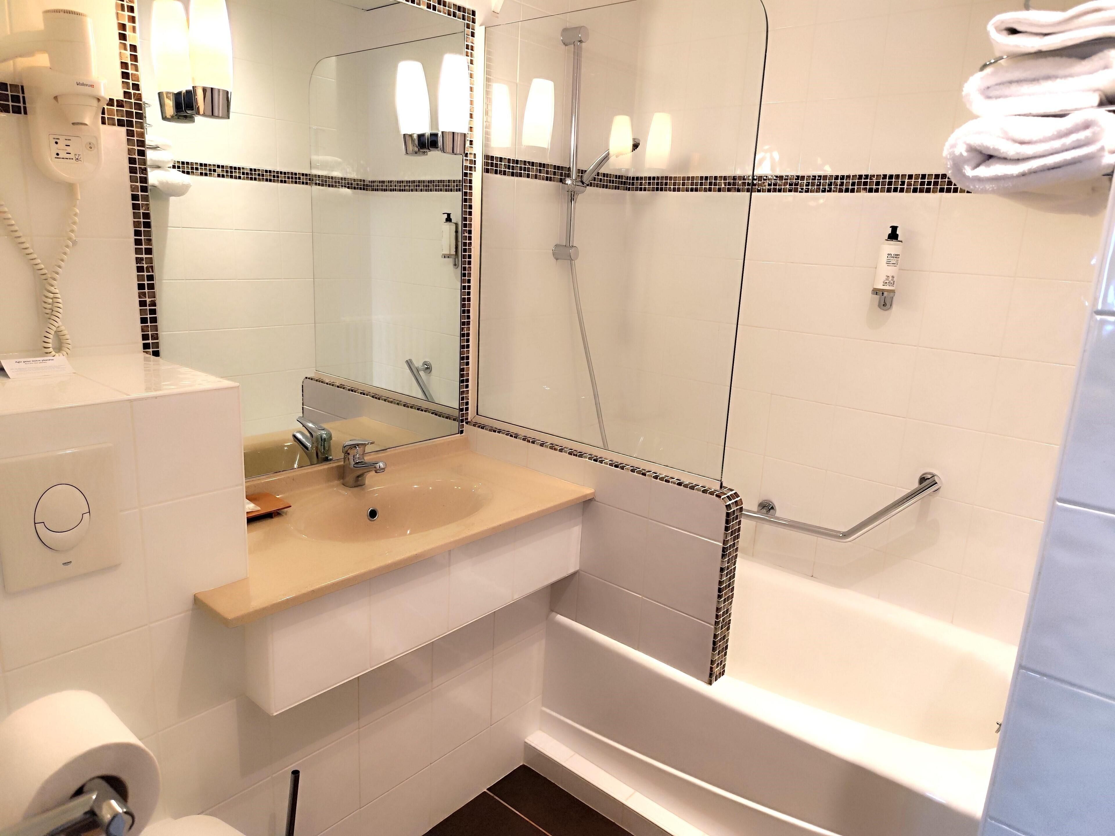 A bathroom with a sink, mirror, hairdryer, and a bathtub.