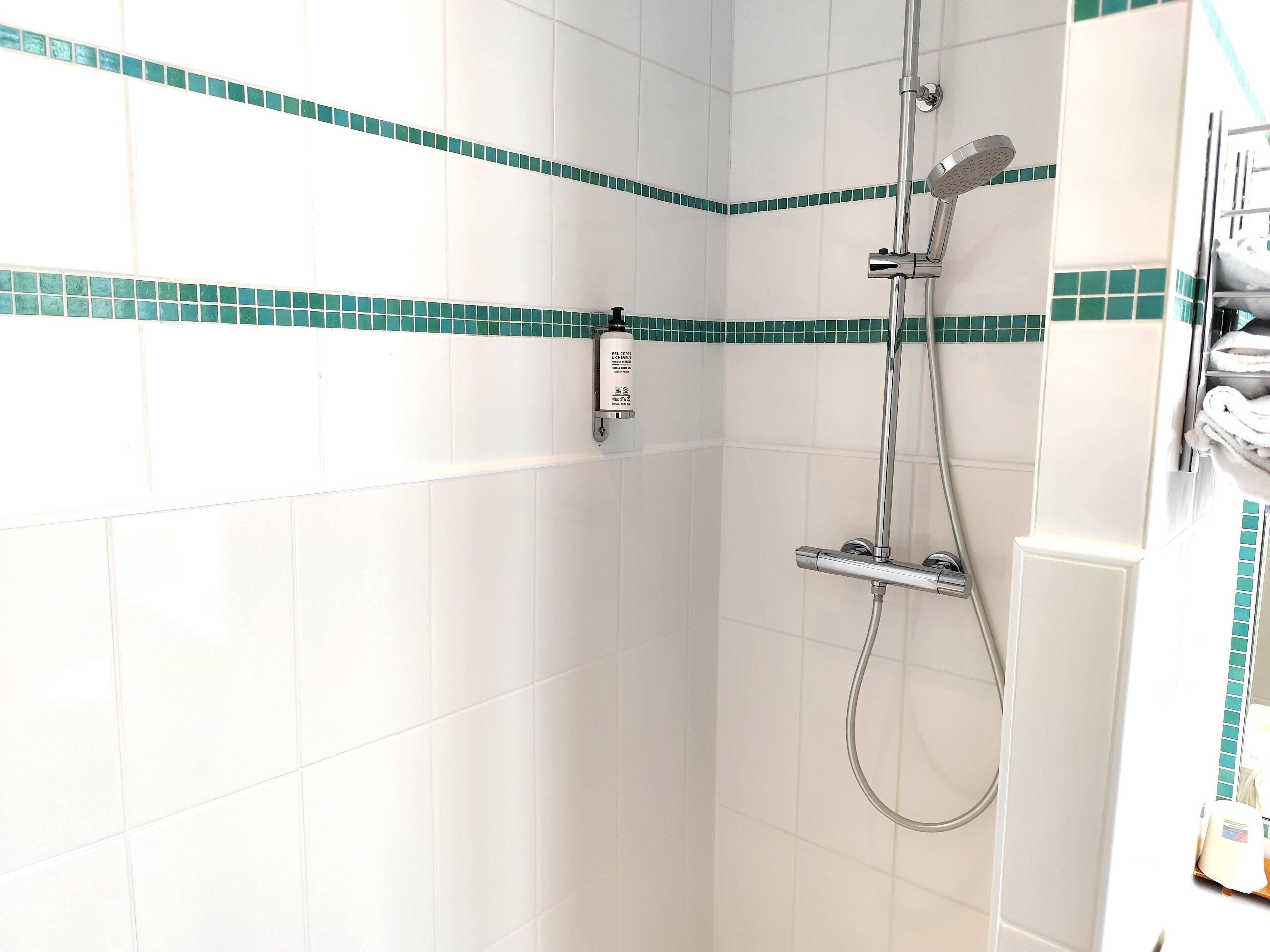 A shower with a handheld showerhead and a wall-mounted faucet, a towel rack, and a soap dispenser on the wall.
